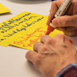 zwei Hände, schreibend auf gelbe Ideenkarten